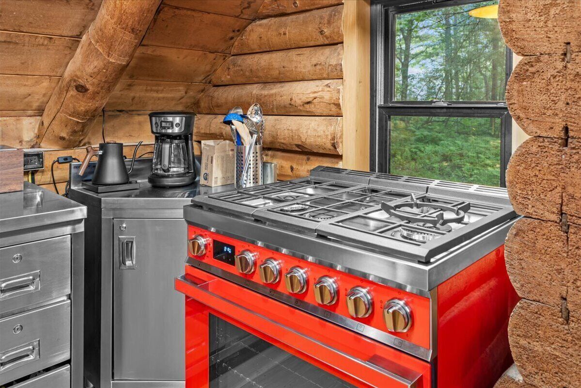 A kitchen with a red stove, a coffee maker, and a window with a view of trees.