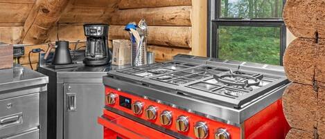 A kitchen with a red stove, a coffee maker, and a window with a view of trees.
