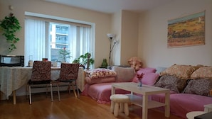 A living room with a sofa, a table, a chair, a small stool, a microwave, and a window with blinds. - Cozy Home in Vancouver (Vancouver)