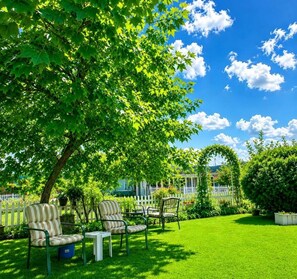 Ein gepflegter Garten mit Rasen, einem weißen Zaun und einem Baum, der Schatten spendet.