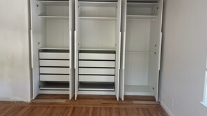 A walk-in closet with open doors, wooden flooring, and a ceiling light fixture.