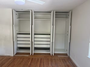 A walk-in closet with open doors, wooden flooring, and a ceiling light fixture.