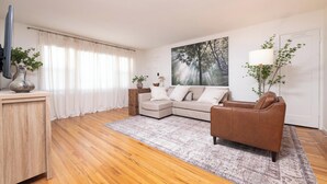 A living room with a sectional sofa, a coffee table, a TV, and a large painting on the wall.