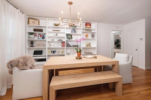 Un salon moderne avec une table à manger en bois, des canapés blancs, une bibliothèque et un lustre.