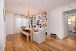 A dining area with a wooden table, chairs, and a bookshelf filled with various items.
