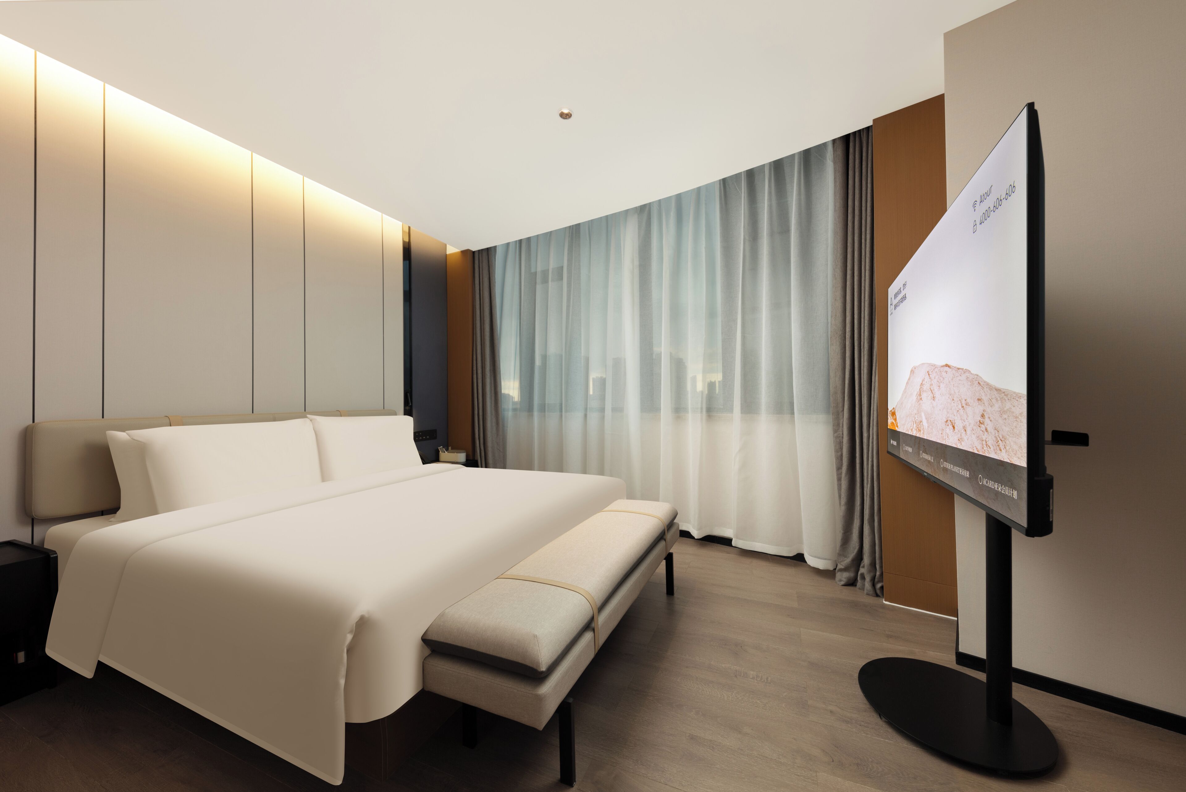 A modern hotel room with a large bed, a flat-screen TV, and a city view.