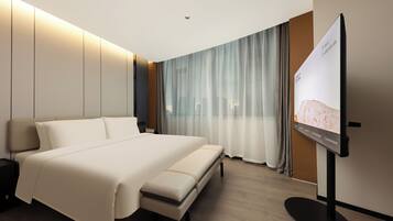 A modern hotel room with a large bed, a flat-screen TV, and a city view.