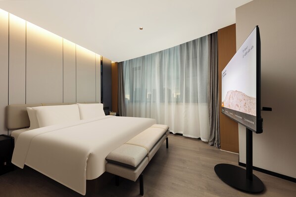 A modern hotel room with a large bed, a flat-screen TV, and a city view.