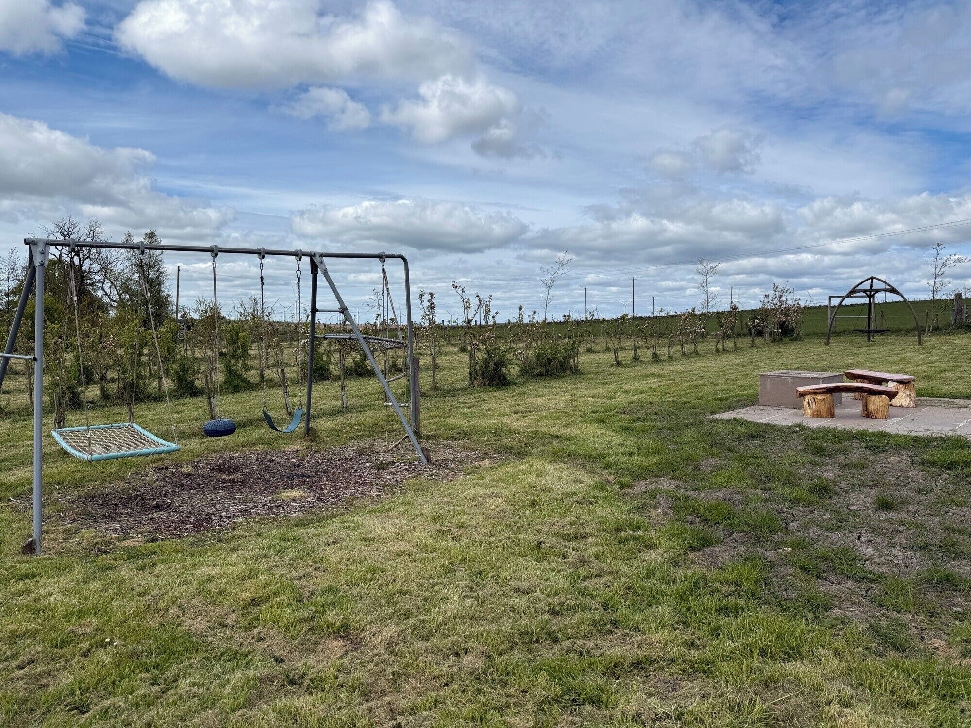 A playground with swings and a seesaw, surrounded by grass and trees.