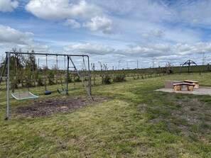 A playground with swings and a seesaw, surrounded by grass and trees.