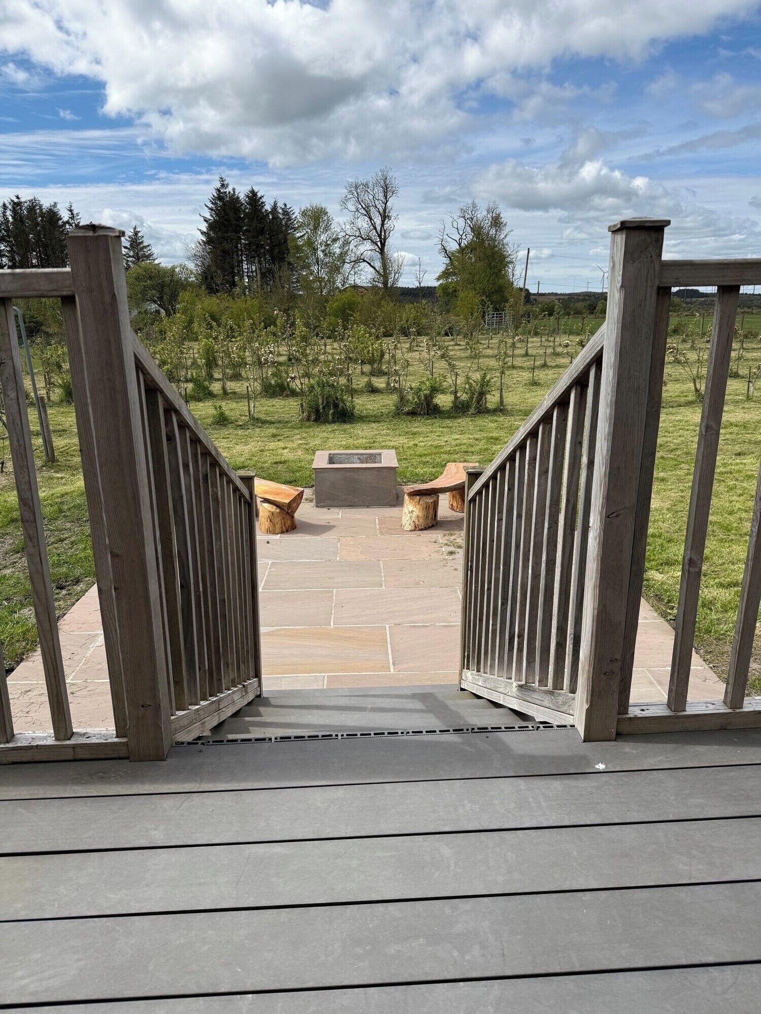 Une terrasse en bois avec un chemin de pierre menant à un espace de détente équipé de bancs et d’un foyer.