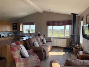 A spacious living area with a kitchen, a fireplace, and large windows offering a view of the outdoors.