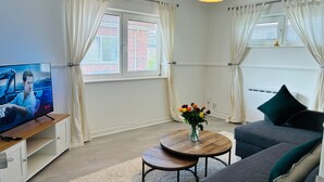 A modern living room with a television, a round coffee table, a sofa, and a decorative vase with flowers. - Cozy Grays Apartment (Grays)