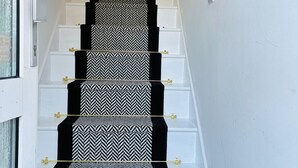 A staircase with a black and white patterned carpet, white walls, and a wooden handrail. - Cozy Grays Apartment (Grays)