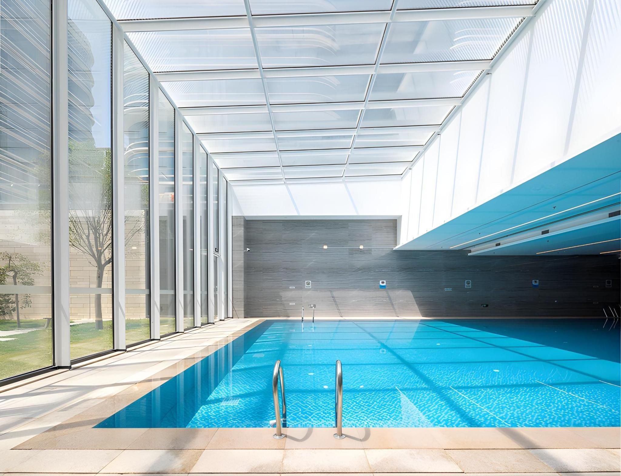 A modern indoor swimming pool with clear glass walls, a tiled floor, and a view of the outdoors.