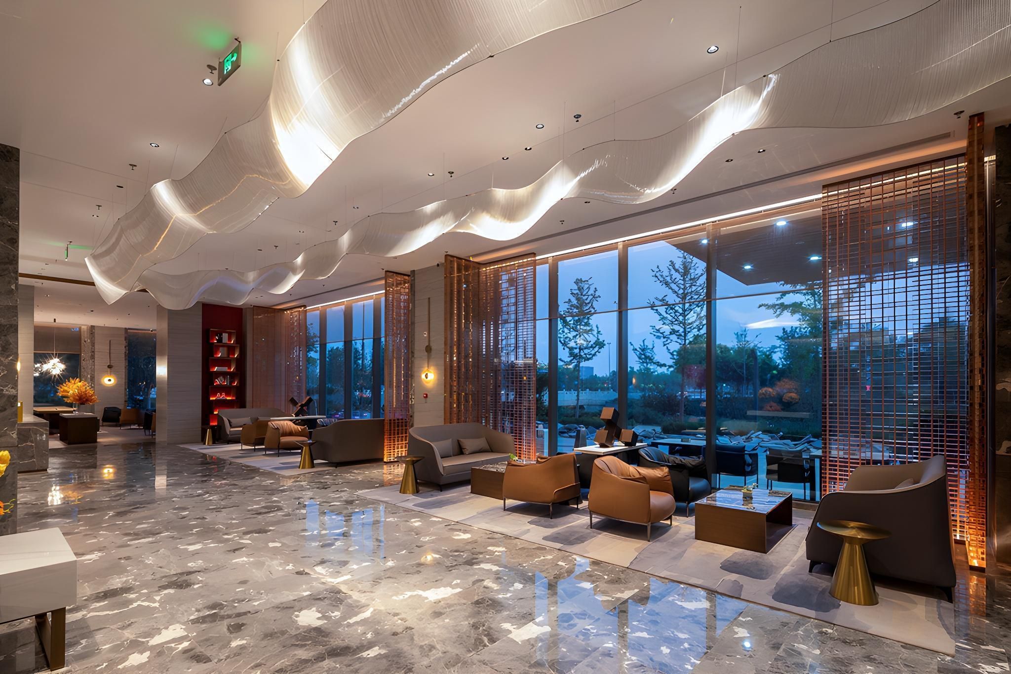A modern lobby with a marble floor, seating areas, and large windows offering a view of the outdoors.