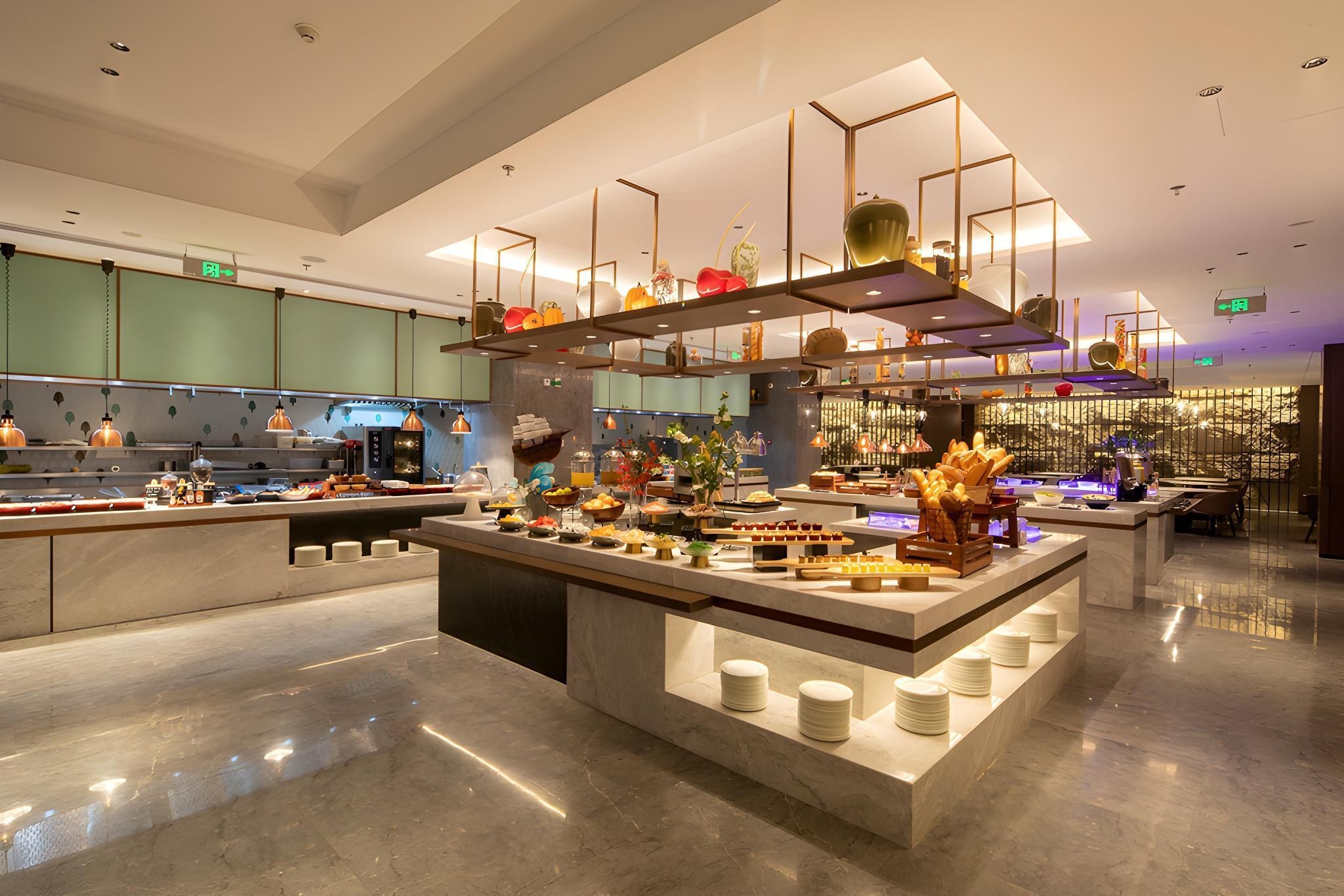 A modern hotel lobby with a central island featuring a buffet, surrounded by seating areas and a kitchen in the background.