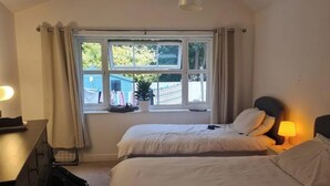 A hotel room with two beds, a desk, a lamp, and a window with curtains. - 1 Bed - Sleeps 2 plus child - Garden - Pets (Bristol)