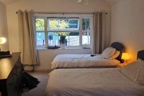 A hotel room with two beds, a desk, a lamp, and a window with curtains. - 1 Bed - Sleeps 2 plus child - Garden - Pets (Bristol)