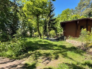 A wooden cabin with a stone foundation, surrounded by dense greenery and trees. - A cozy log cabin with a sauna and fireplace right next to the forest (Karwitz)