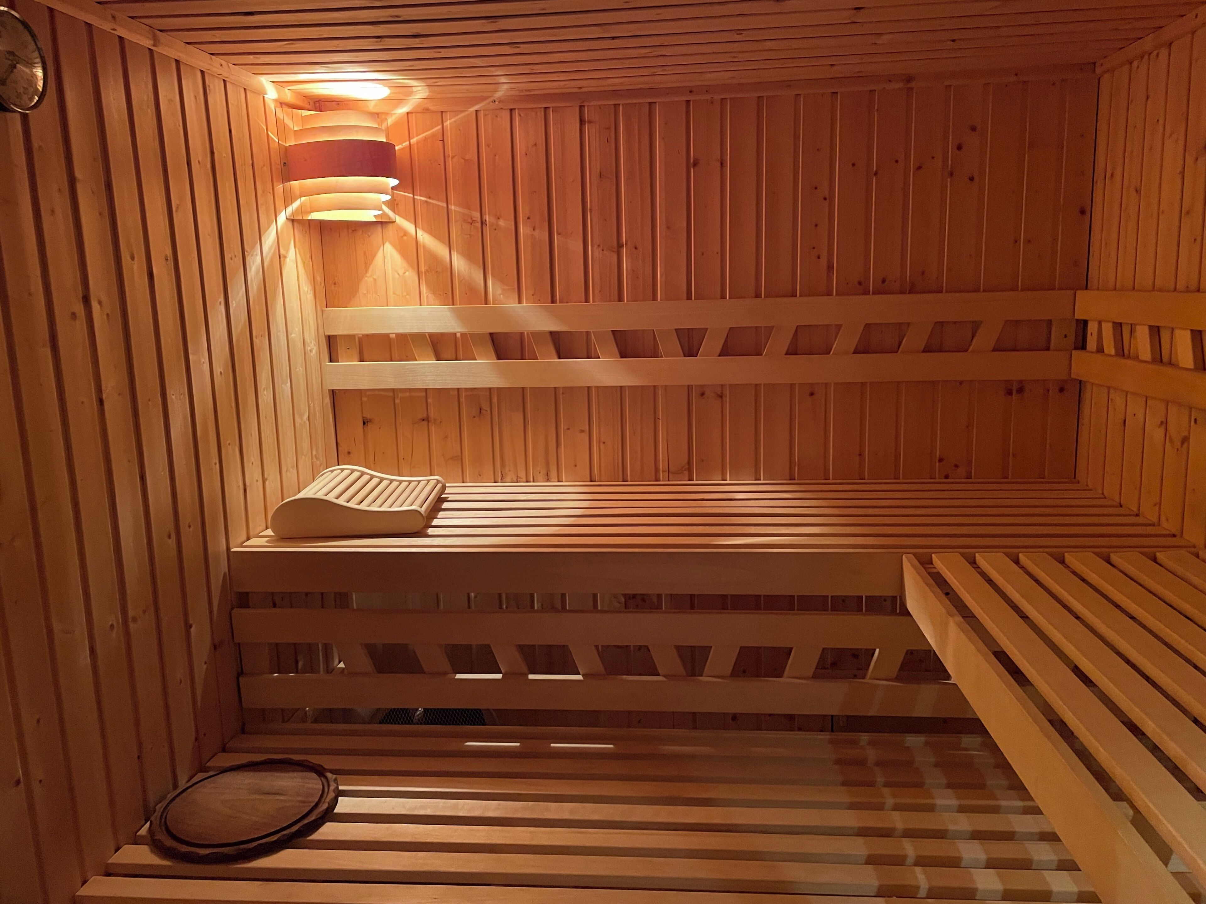 Un sauna avec des bancs en bois et une banquette, un radiateur fixé au mur et une horloge.