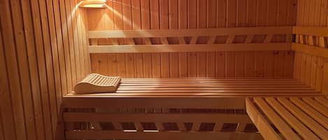 Un sauna avec des bancs en bois et une banquette, un radiateur fixé au mur et une horloge.