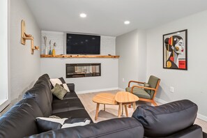 A modern living room with a black leather sofa, a wooden coffee table, a fireplace, and a mounted TV.