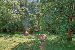 A forested area with a fire pit surrounded by chairs.