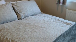 A bed with a patterned bedspread and pillows, a window with curtains, and a radiator.