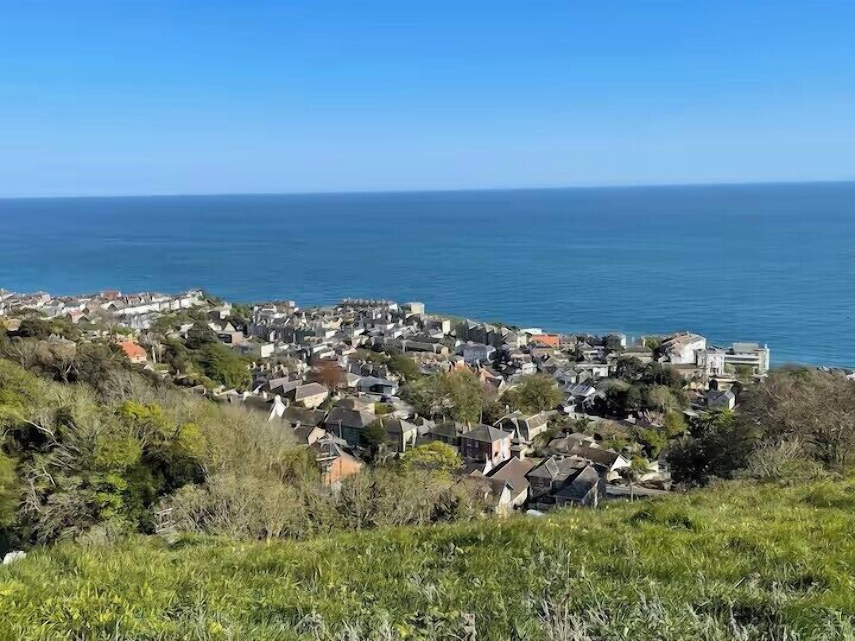 A coastal town with houses and buildings, a clear sky, and the sea in the background.