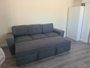 A grey sectional sofa in a room with a white wardrobe and a white door marked 'First Aid'.