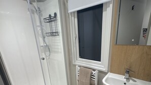 A bathroom with a glass shower enclosure, a white sink, a towel rack, and a window with a view. - Sleeps6-BeachCaravan-FreeParking-Porthcawl (Porthcawl)