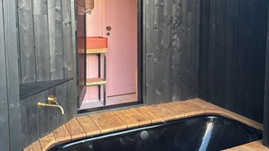Una habitación de madera con una bañera negra, un banco de madera y una pequeña mesa.