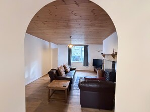 A living room with a wooden ceiling, a sofa, a coffee table, a fireplace, and a television.