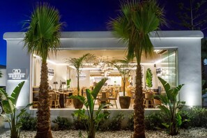A modern restaurant with a patio area, visible seating, and a sign indicating it is a dining establishment. - Aeolos Resort (Mykonos)