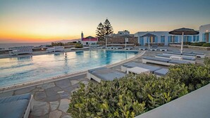 A pool area with lounge chairs and a view of the sunset. - Aeolos Resort (Mykonos)