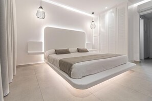 A modern bedroom with a built-in bed, bedside tables, and pendant lighting. - Aeolos Resort (Mykonos)