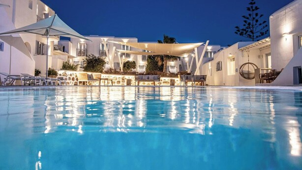 A swimming pool with lounge chairs and umbrellas, surrounded by white buildings with balconies. - Aeolos Resort (Mykonos)