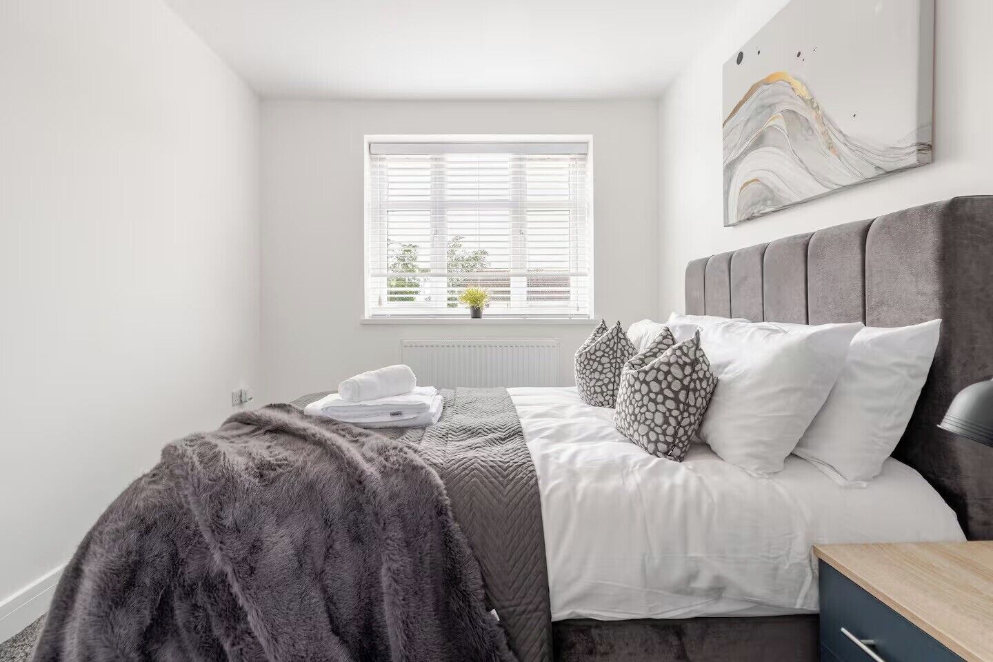 A bedroom with a bed, a window with blinds, a radiator, and a wall-mounted artwork.