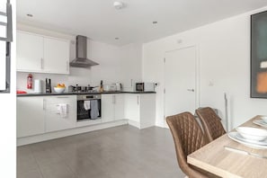 Eine moderne Küche mit weißen Schränken, einem Herd, einem Backofen und einem Essbereich mit Tisch und Stühlen.