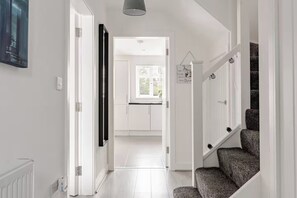 Un couloir avec un escalier, un radiateur et une porte donnant sur une pièce avec une fenêtre.