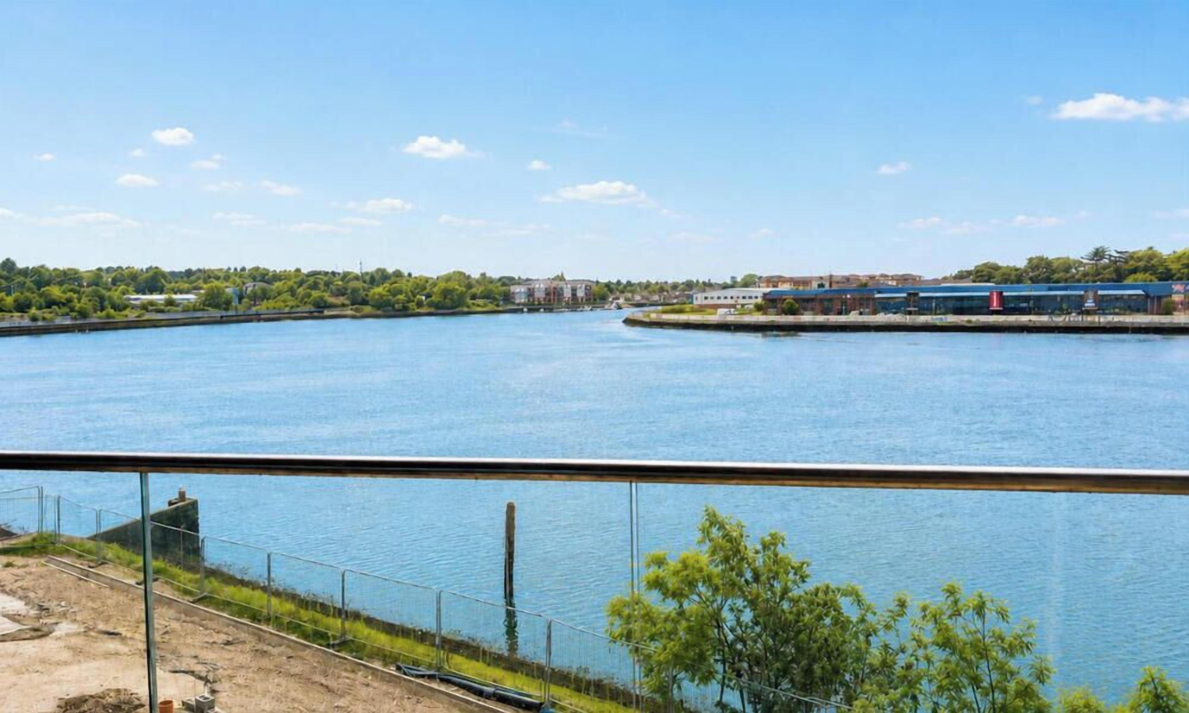 A waterfront view with a clear sky, a body of water, and a distant building complex.