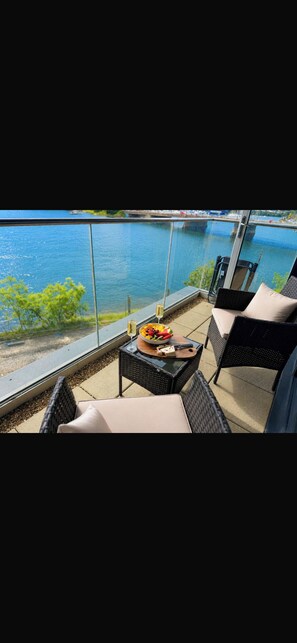 Ein Balkon mit Korbmöbeln, einem Glastisch und einer Schüssel mit Obst und Käse.
