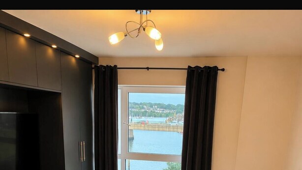 A bedroom with a bed, a TV, and a view of a body of water through a window. - Southampton 2-Bed Apartment, Sleeps 4 with Balcony (Southampton)