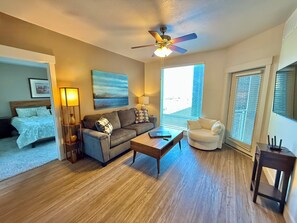 A living room with a sofa, coffee table, and a chair. There is a ceiling fan, a painting on the wall, and a window with blinds. - Spacious 2-bedroom Executive Condo (Salt Lake City)