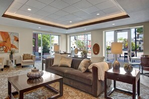 A spacious living area with a large sofa, a coffee table, and a side table with a lamp. Large windows provide a view of the outside. - Spacious 2-bedroom Executive Condo (Salt Lake City)