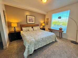 A bedroom with a bed, two bedside tables, a nightstand, a window with blinds, and a floor lamp. - Spacious 2-bedroom Executive Condo (Salt Lake City)