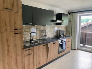 A modern kitchen with wooden cabinets, a black countertop, a built-in oven, and a window with a view of the outdoors. - Appartements Konrad (Soell)