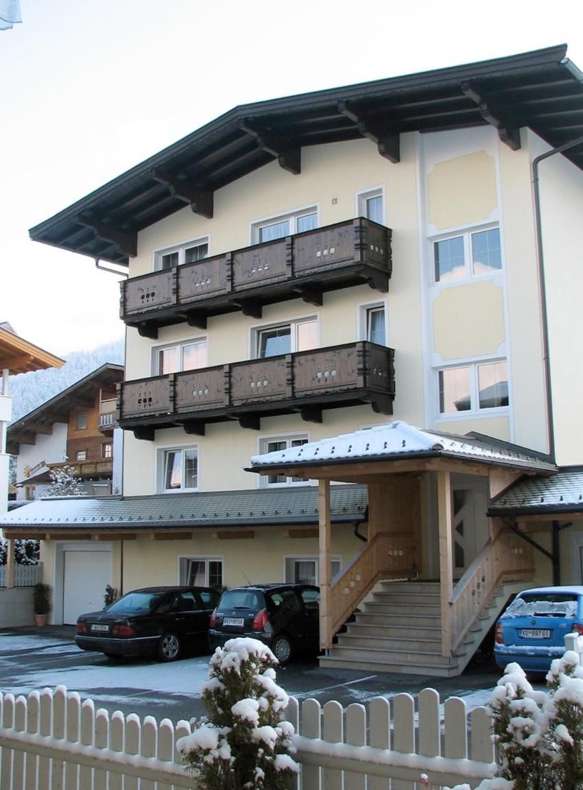 Ein mehrgeschossiges Gebäude mit Balkonen, einer überdachten Eingangspforte und Autos vor der Fassade.