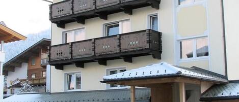 Un edificio de varios pisos con balcones, un acceso cubierto y coches estacionados al frente.
